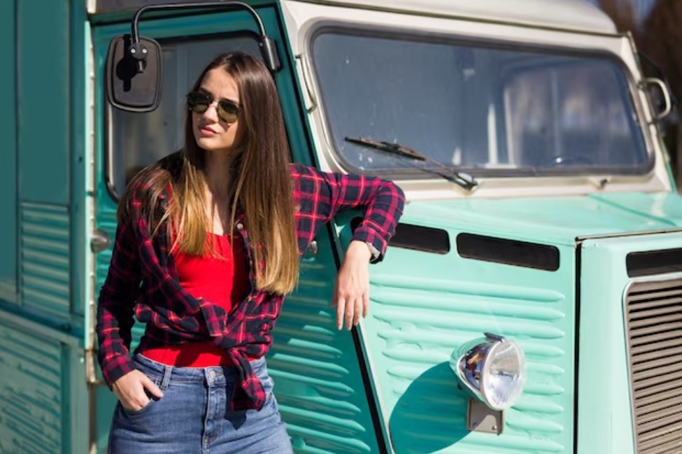 a girl wearing glasses leaning on an old bus colored in turquoise