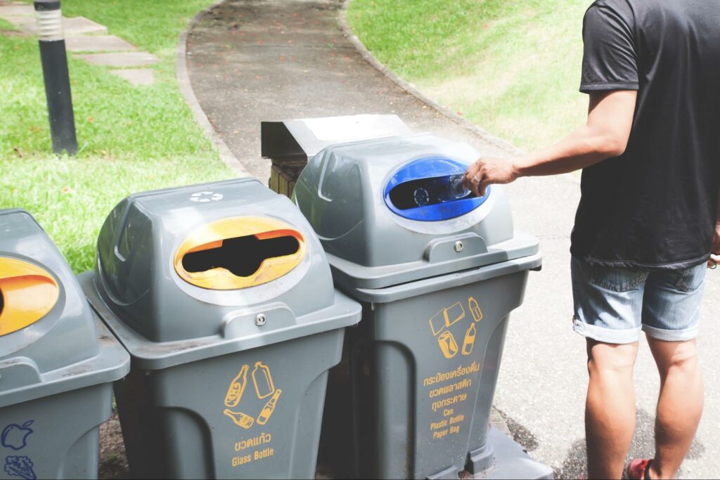 a man putting a glass bottle in a recycle trash bin