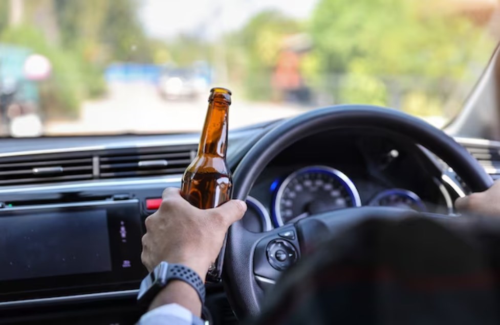 man holding a bottle and driving a car